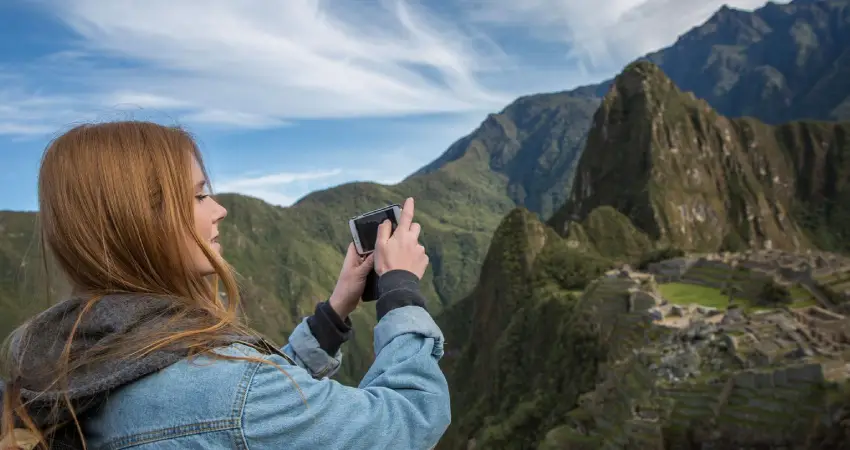 A woman captures a photo of Machu Picchu mountain during her Peruvian Amazon tour from Cusco.