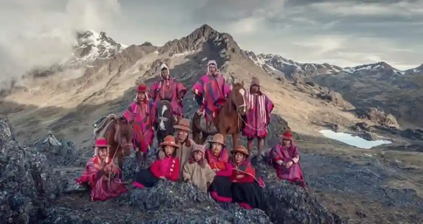 A group of individuals in traditional Qeros clothing stands atop a mountain, showcasing their cultural heritage against a scenic backdrop.