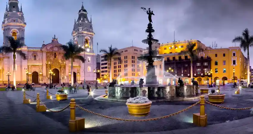 A vibrant city square showcasing a fountain, with a grand cathedral behind it, reflecting the pleasant August weather in Peru.