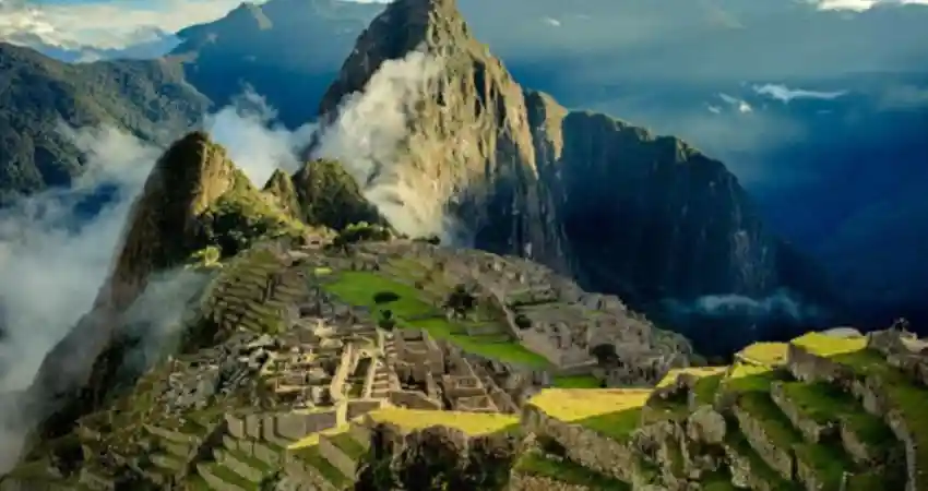 The ruins of Machu Picchu in Peru, surrounded by lush greenery under a clear August sky, showcasing ancient Incan architecture.